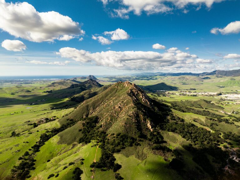 Aerial view of green rolling hills and volcanic peaks near San Luis Obispo under a blue sky with clouds